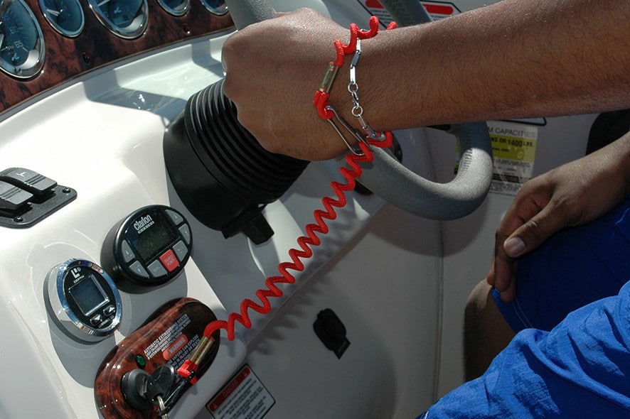 A man is operating a boat while using an Engine Cut-Off Switch attached to the steering wheel.