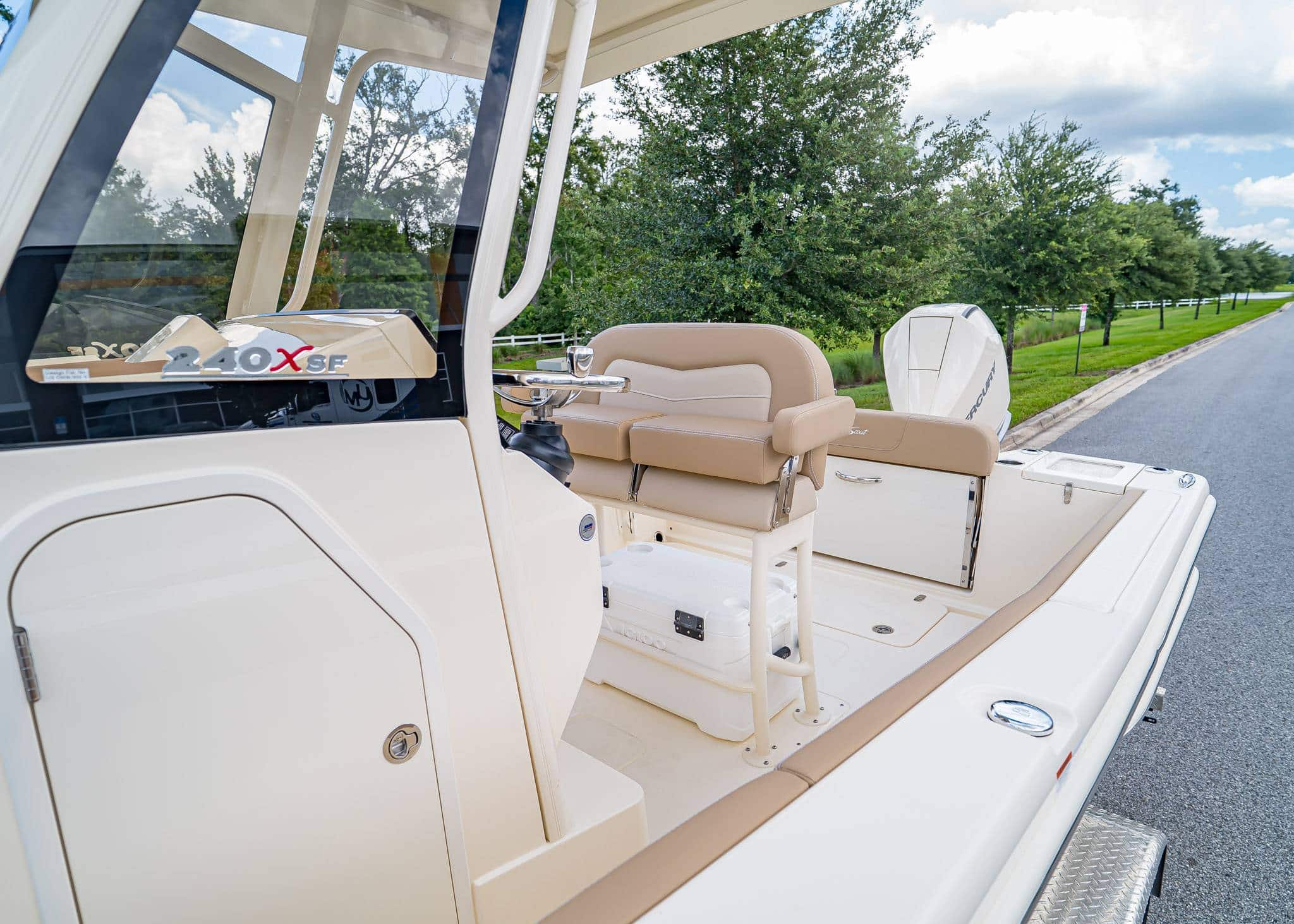 Overhead view of a Scout 215’s bow seating area with light beige cushioned seats, a center console, and stainless steel handrails, docked near grass and pavement.